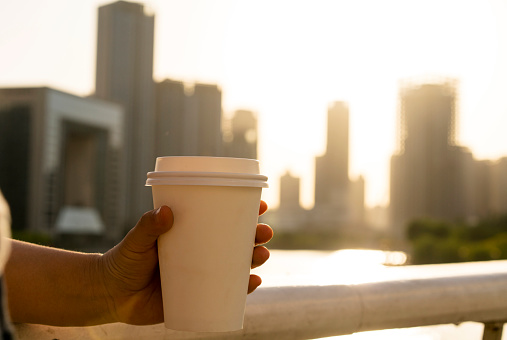 girl holding coffee cup, enjoying the city skyline at sunset