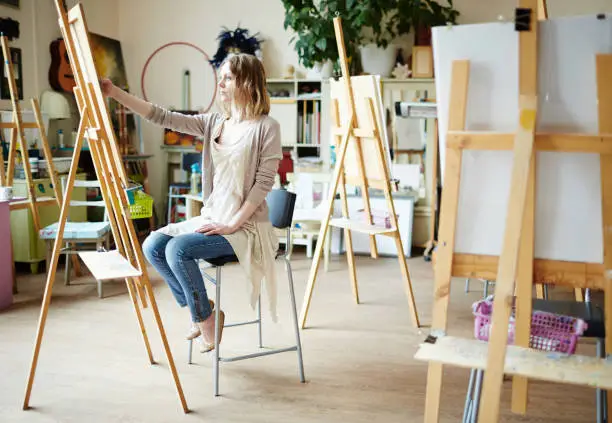 Serious girl sitting in front of easel and drawing