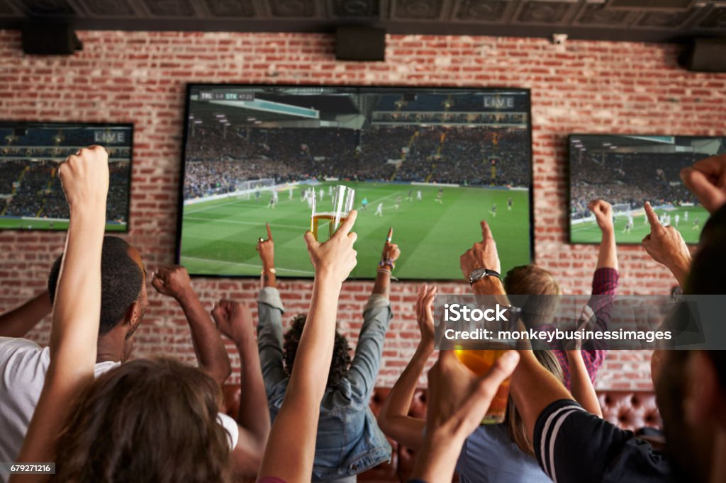 Vue arrière des amis regardant le jeu dans le bar de sports sur des écrans - Photo de Bar libre de droits