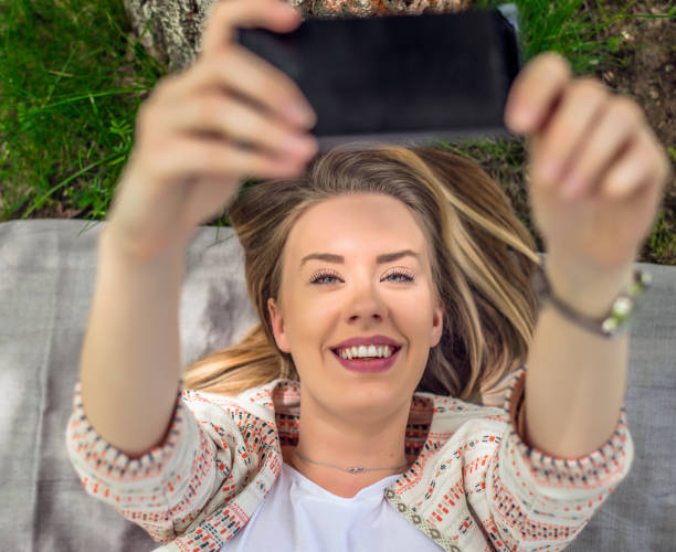 istock woman lying in grass taking selfie with smart phone 679281182
