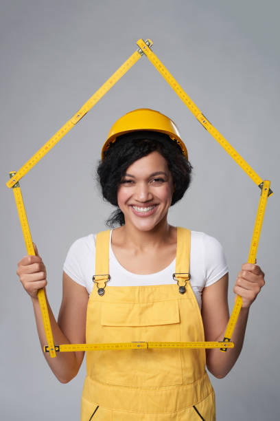 Builder in yellow helmet and overall showing a house frame