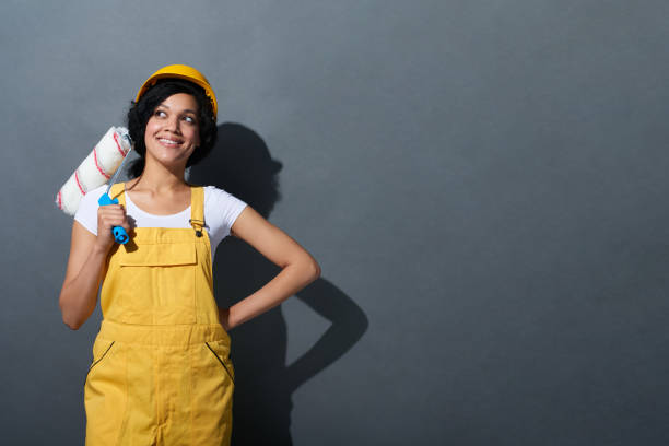 happy smiling woman builder wearing yellow protect helmet - female house painter home decorator paintbrush imagens e fotografias de stock