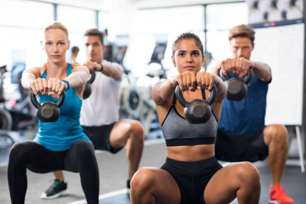 People with kettlebells squatting Women and men exercising with kettlebells in gym. Group of young people doing a kettle bell exercise along with squatting. Fitness class and girls training by weights. kettlebell stock pictures, royalty-free photos & images