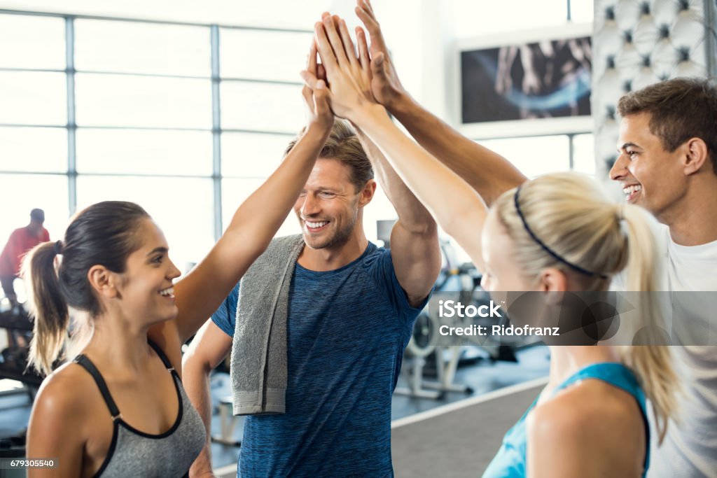 High five at gym Smiling men and women doing high five in gym. Group of young people making high five gesture in gym after workout. Happy successful fitness class after training. Health Club Stock Photo