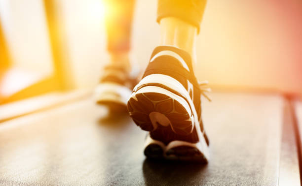 Fitness girl running on treadmill at gym. Rear view of detail of feet of young woman wearing sneakers and running on treadmill. Fitness and healthy lifestyle concept.