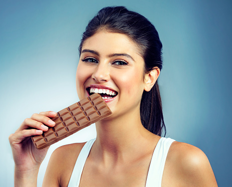 Portrait of an attractive young woman eating a chocolate against a blue background