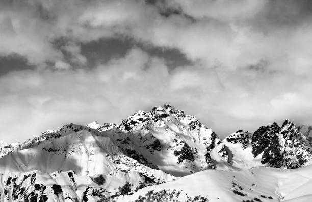 istock Black and white snow slope and winter sunlight mountains in clouds 679353364