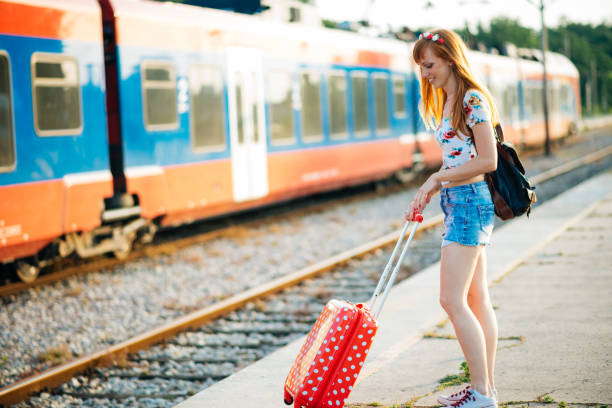 Beautiful young fashionable woman with a suitcase waiting for a train at the railroad station on a sunny day