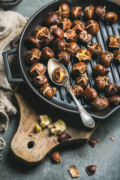 geröstete kastanien aus gusseisen pfanne über holzbrett grillen - nut cracked roasted food stock-fotos und bilder