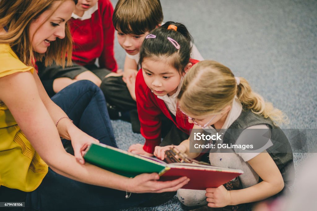 Storytime In The Classroom Teacher is sitting in the classroom with her primary school students, reading a story to them. Storyteller Stock Photo