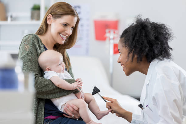 Happy doctor check's baby's reflexes Cheerful African American female pediatrician uses a reflex hammer to check baby's reflexes. The baby's mother is holding her. rubber mallet stock pictures, royalty-free photos & images