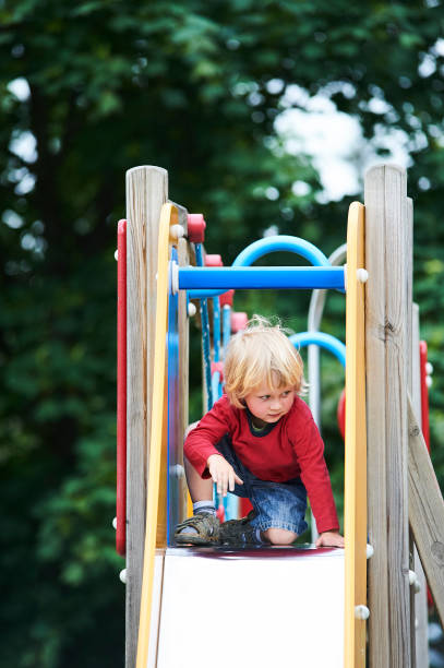 istock Little child blond boy sliding down a slide at the summer playground 679456980