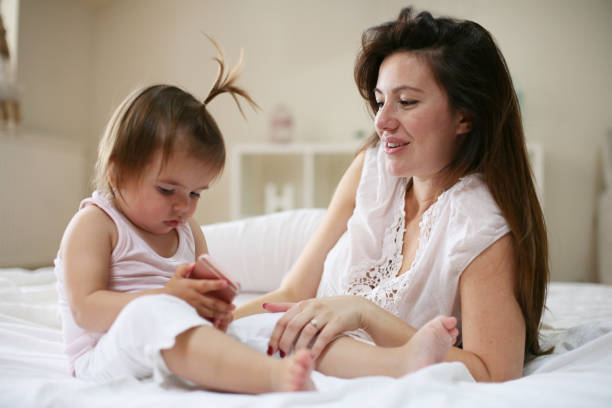 istock Mother with her little baby having fun in the bed. Using smart phone. 679460314