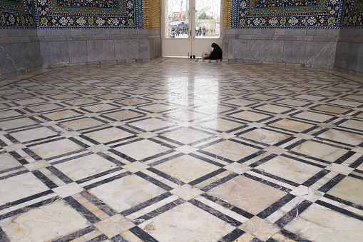 Woman in black hijab siting on the nice squares texture ground in a mosque in Qom, Iran