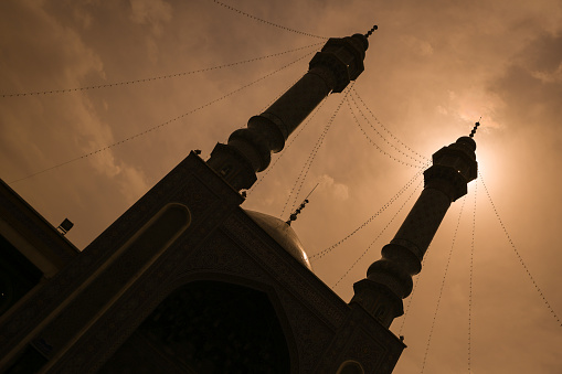 Black mosque silhouette with two minaret towers in a golden sky background in Qom, Iran