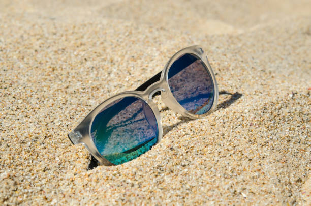 istock Sunglasses on the beach. Multi colored stylish model with transparent frame and blue lenses. Vacation concept. 679480112