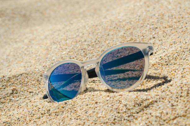 istock Sunglasses on the beach. Multi colored stylish model with transparent frame and blue lenses. Vacation concept. 679480172