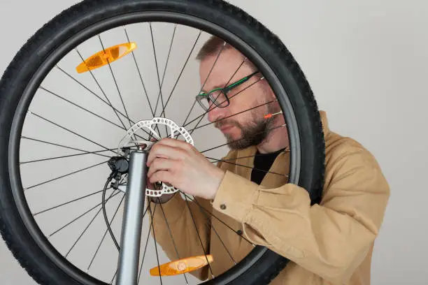 Bearded man screws  the front wheel with hydraulic disc brake on the mtb bicycle.