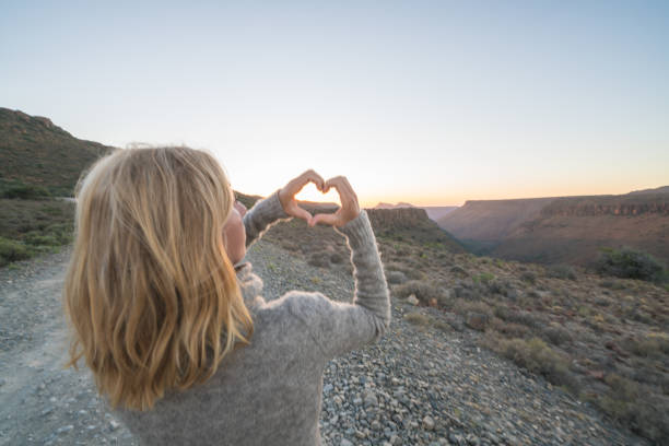 istock Young woman making heart shape frame on landscape 679486272