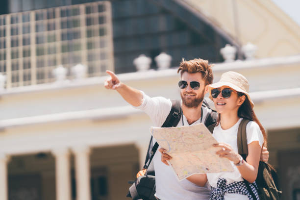 Multiethnic traveler couple using generic local map together on sunny day, man pointing toward copy space. Honeymoon trip, backpacker tourist, Asia tourism, or holiday vacation travel concept
