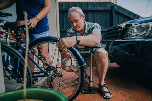 A father inflating the tire of his wife's bicycle in the entrance to their garage.