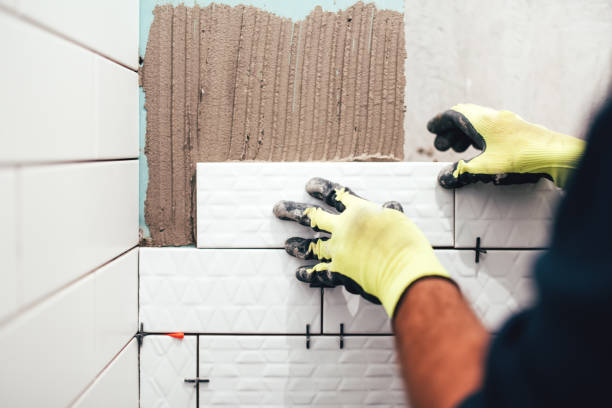 construction worker installing small ceramic tiles on bathroom walls and applying mortar with trowel stock photo