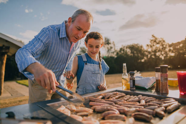 aiutare papà a cucinare salsicce sul barbecue - grilled foto e immagini stock