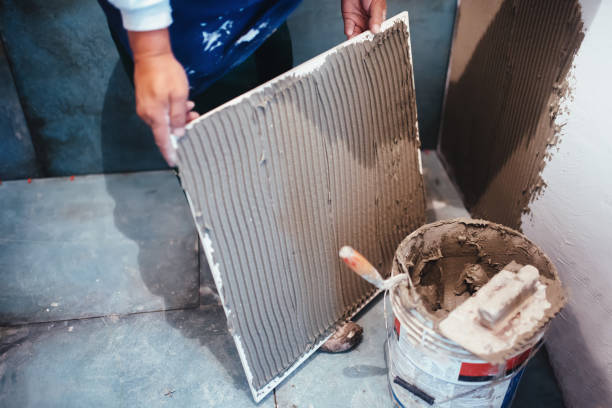 istock Industrial worker installing bathroom ceramic floor tiles, adding flexible cement adhesive with comb trowel 679512276