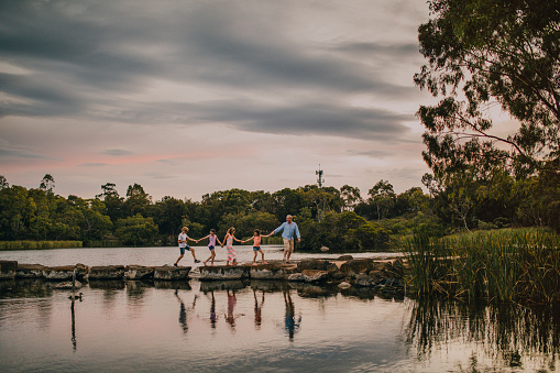 Family and friends jumping on the stepping stones across the centre of the Newport Lakes Reserve.