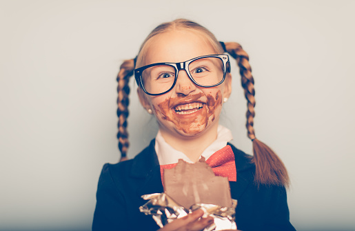 A young girl nerd is eating a chocolate bar and the sugar has gone to her head. She has smeared chocolate all over her face and doesn't know what to do with herself as she loves chocolate so much. This might be a problem.