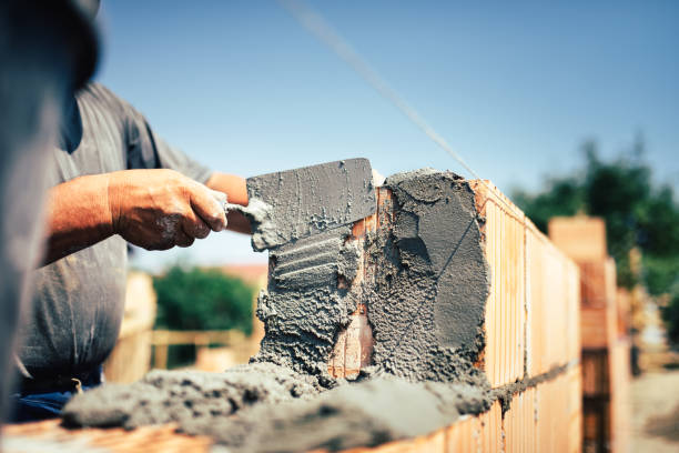 Bricklayer construction worker installing brick masonry on exterior wall with trowel putty knife stock photo