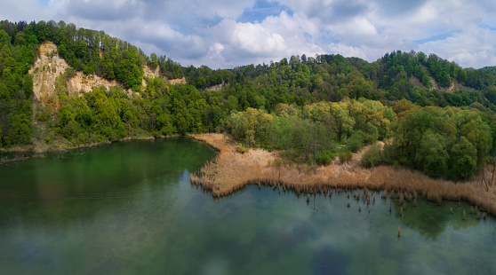Panorama picture of a  lake and green hlills with a steepface . Clouds reflecting in the water. Picture made with a drone.