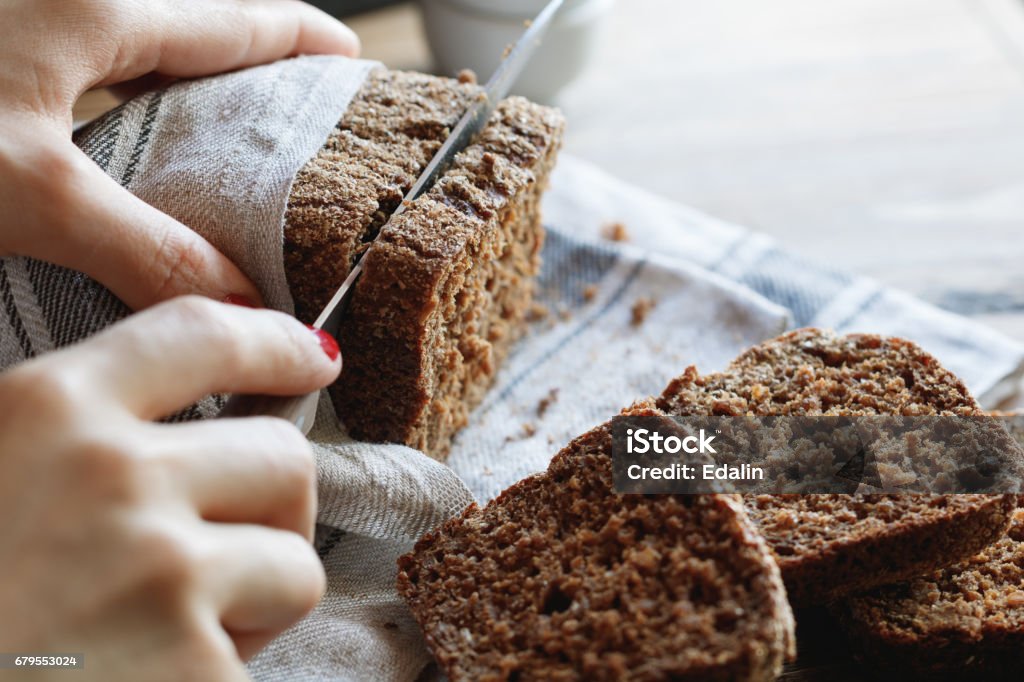 La jeune fille coupe pain de seigle complet sur une table en bois. - Photo de Pain libre de droits