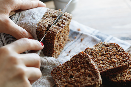 The girl cuts whole-wheat rye bread on a wooden table.