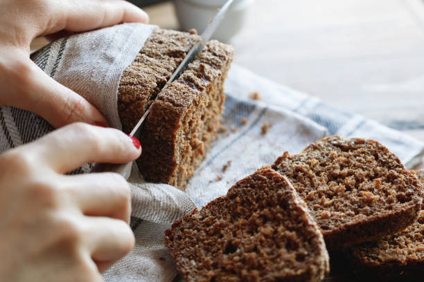 the girl cuts whole-wheat rye bread on a wooden table. - home made bread imagens e fotografias de stock