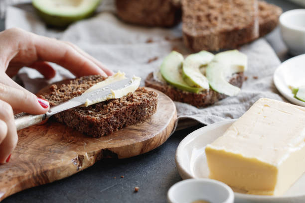 The girl is preparing toast from rye bread and butter for breakfast. The girl spreads butter on whole wheat rye bread. spread food stock pictures, royalty-free photos & images