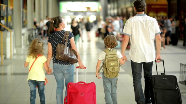 Happy family with little girl and boy going on railway station, mother father and the kids walk through the airport with suitcases
