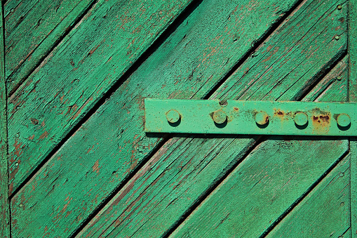 A fragment of an old, painted, wooden door with hinges