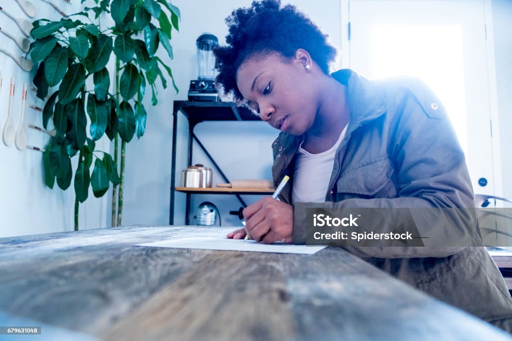 African American Woman Fills out Form Millennial female black woman fills out a job application at a wood work table. Form Filling Stock Photo