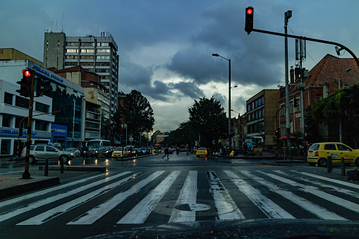 Bogotá, Colombia - May 05, 2017: The Driver's view on Carrera Septima in the Chapinero area of the  capital city of Bogota in the South American country of Colombia. It has been raining and the road is wet. The sky is still heavily overcast. The car has come to a halt at the Traffic Lights, giving the driver the opportunity to shoot the image. On either side of the road are office and apartment buildings. The elevation at street level is about 8500 feet above mean sea level. Horizontal format. Copy space.