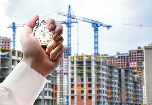 Buildings under construction with cranes and stopwatch in male hand