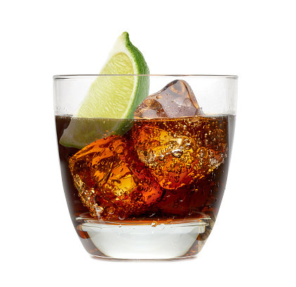 Cuba libre rum cocktail with ice cubes and lime wedge isolated on white background