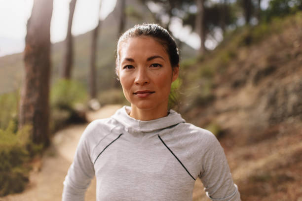 Woman runner standing outdoors on country road Portrait of young female athlete standing outdoors and looking at camera. Woman runner outdoors on country road taking a break after running exercise. determination asian stock pictures, royalty-free photos & images
