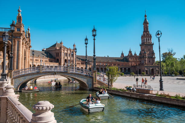 touristen paddeln ruderboote im kanal rund um die gebäude in der plaza de espana in sevillia andalusien - plaza de espana european culture sevilla seville stock-fotos und bilder