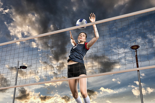 Female volleyball player hitting the ball in the air on cloudy sky background