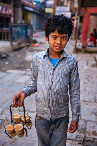 Indian little boy selling  tea - masala chai on streets of Kathmandu, Nepal. Masala chai is a beverage from the Indian subcontinent made by brewing tea with a mixture of aromatic Indian spices and herbs