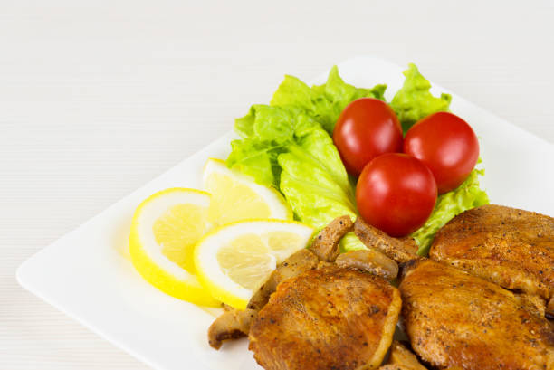 Pork fillet steak with cherry tomatoes, lemon and a lettuce in white dish on white background.