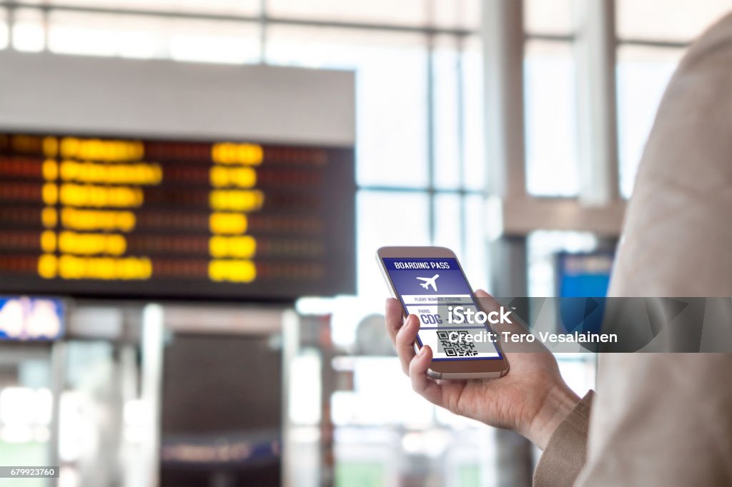 Boarding pass in smartphone. Woman holding phone in airport with mobile ticket on screen. Modern travelling technology and easy access to aeroplane. Terminal and timetable in the blurred background. Transportation and mobile services Airplane Ticket Stock Photo