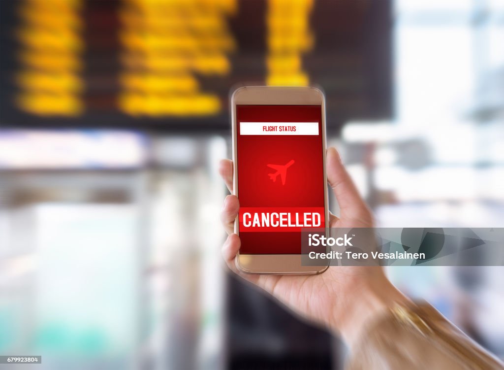 Flight cancelled. Smartphone application announces bad news to tourist. Strike or problem with plane. Woman holding mobile phone in airport terminal. Timetable and schedule in the blurred background. Transportation and mobile services Commercial Airplane Stock Photo