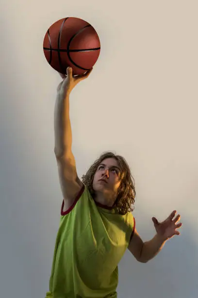 Young boy with long blond hair playing basketball in a striking position with a green jersey on.